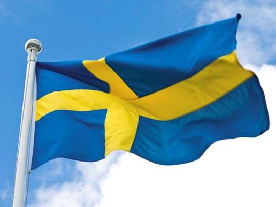 Den blågula svenska flaggan som vajar i vinden mot blå himmel och vita moln